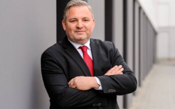 Sven Oldenburg, Direktor Core Banking bei adesso, präsentiert sich in formeller Kleidung mit verschränkten Armen vor einer modernen Architektur. Die Darstellung unterstreicht seine Expertise in der Legacy-Modernisierung und der Sidecar-Architektur im Finanzsektor.