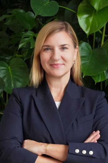 Vanessa Müller, Partnerin im Consulting-Bereich bei EY Luxemburg, präsentiert sich vor einer grünen Pflanzenkulisse. Ihr professionelles Auftreten spiegelt die Relevanz von Echtzeitzahlungen in der EU wider, insbesondere im Kontext der neuen regulatorischen Anforderungen.