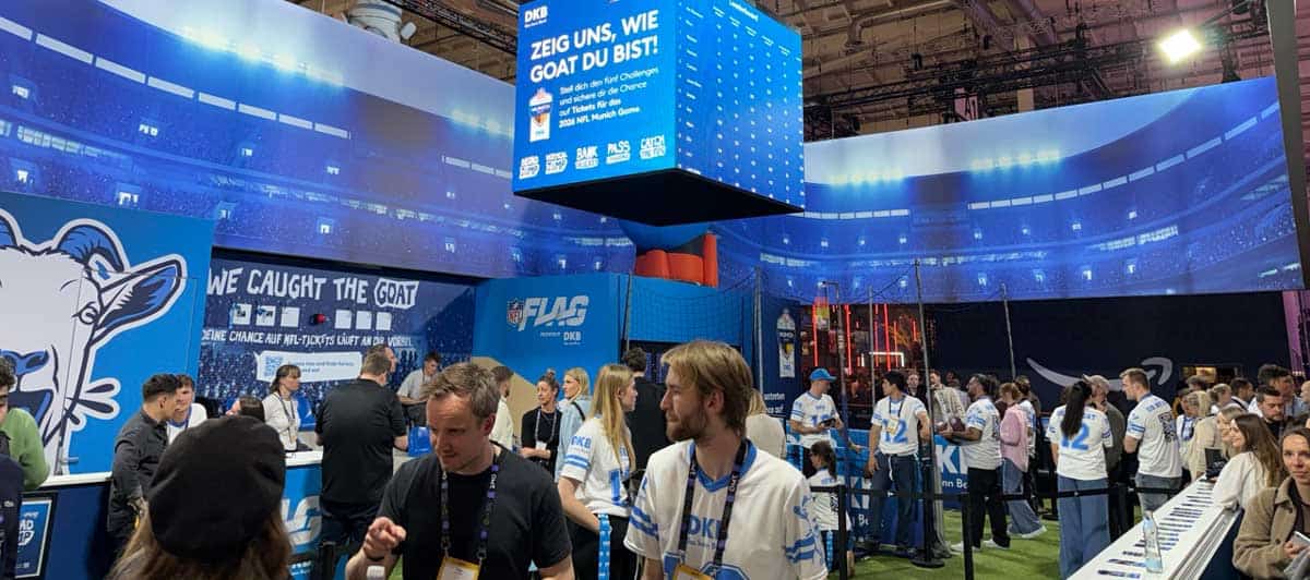 Am Stand von DKB beim OMR-Festival 2026 interagieren Besucher mit verschiedenen Aktivitäten. Eine große digitale Anzeige informiert über die NFL-Challenge. Die Atmosphäre ist lebhaft, mit Teilnehmern in Sporttrikots und einem ansprechenden Design im Hintergrund.