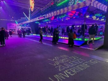 Das OMR-Festival 2026 präsentiert eine lebhafte Atmosphäre mit bunten Lichtern und zahlreichen Besuchern. Im Vordergrund ist eine beschriftete Fläche sichtbar, die zur Reflexion anregt. Porsche ist als Partner des Festivals vertreten.