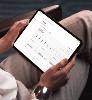 Ein Tablet wird gehalten, auf dem eine Benutzeroberfläche mit Finanzdaten angezeigt wird. Die Darstellung umfasst verschiedene Währungsbeträge und Diagramme. Santander ist als Hauptanteilshaber an Ebury beteiligt, das internationale Zahlungslösungen anbietet.