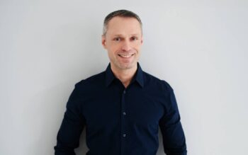 Gerrit Meier, Chief Commercial Officer der Hanseatic Bank, lächelt in die Kamera. Er trägt ein dunkles Hemd und steht vor einer hellen Wand. Seine Position umfasst die Vermarktung von Finanzprodukten, einschließlich Kreditkarten.