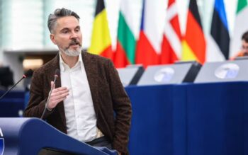 Fabio De Masi, Mitglied des Ausschusses für Wirtschaft und Währung des Europäischen Parlaments, spricht über die Herausforderungen der digitalen Souveränität Europas im Finanzsystem. Im Hintergrund sind Flaggen europäischer Staaten sichtbar.