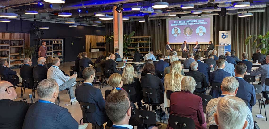 Im Rahmen von CIBI 2026 diskutieren Experten auf einer Bühne über digitale Souveränität und Herausforderungen im Finanzsektor. Rund 90 Teilnehmer verfolgen die Veranstaltung in einem modernen Veranstaltungsraum, ausgestattet mit technischen Mitteln für die Präsentation.