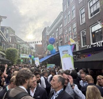 Eine große Menschenmenge versammelt sich in einer belebten Straße während der Money20/20. Bunte Luftballons und Banner sind sichtbar, was auf eine festliche Atmosphäre hinweist. Die Teilnehmer scheinen sich aktiv auszutauschen und zu vernetzen.