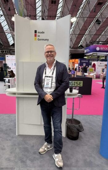 Der Deutsche Pavillon auf der Money20/20 präsentiert sich mit einem "made in Germany"-Schild. Eine Person steht lächelnd vor einem Stand, umgeben von weiteren Ausstellern. Die Atmosphäre ist geschäftig und informativ, ideal für Networking.