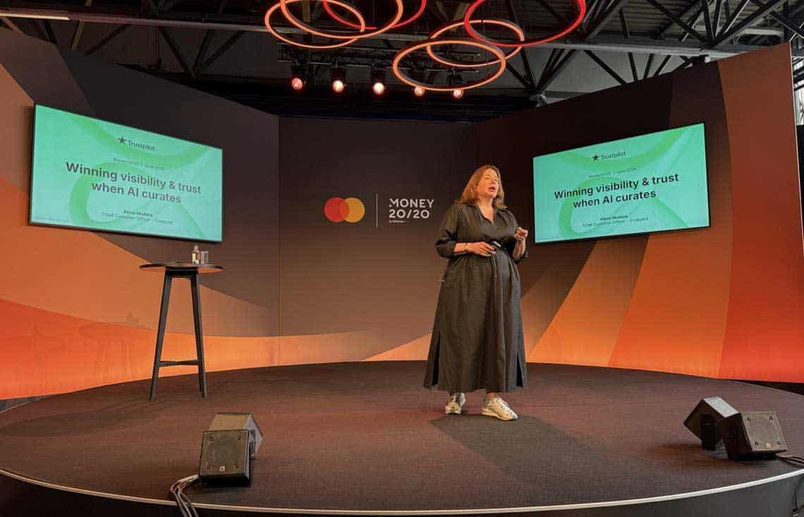 Eine Präsentation auf der Bühne von Money20/20 zeigt eine Rednerin, die über „Winning visibility & trust when AI curates“ spricht. Im Hintergrund sind das Logo von Money20/20 und eine Präsentationsfolie sichtbar.