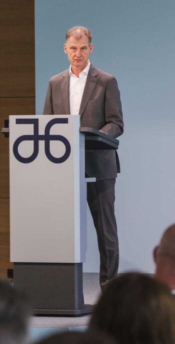 Dr. Markus Wiegelmann, Finanzvorstand und Arbeitsdirektor von Atruvia, steht an einem Rednerpult und präsentiert während der Hauptversammlung. Der Hintergrund ist schlicht gehalten, was die Aufmerksamkeit auf seine Ansprache lenkt.