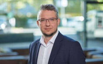 Cedric Heinl, Produktmanager bei KEBA, präsentiert sich in einem professionellen Umfeld. Sein Tätigkeitsbereich umfasst Lösungen im Bargeldmanagement, insbesondere im Bereich der Automatisierung und Self-Service-Technologien für Banken und Finanzinstitute.