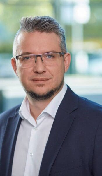 Cedric Heinl, Produktmanager Banking Automation bei KEBA, präsentiert sich in einem professionellen Umfeld. Seine Expertise im Bargeldmanagement unterstreicht die Notwendigkeit mehrschichtiger Sicherheitsmaßnahmen gegen physische Angriffe auf Geldautomaten.