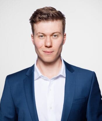 Maximilian Dassler, Senior Product Manager bei DFKP, präsentiert sich in einem formellen Outfit. Der Fokus liegt auf der Bedeutung von Schwellwerten in der KI-Entwicklung, um Prozesse effizienter und kontrollierbarer zu gestalten.