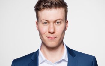 Maximilian Dassler, Autor und Experte im Bereich KI, präsentiert sich in einem formellen Outfit. Der Hintergrund ist neutral, was den Fokus auf die Person lenkt. Die Thematik der Schwellwerte in der KI wird durch seine Expertise unterstrichen.