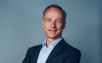 Dirk Littig, Co-Founder und Co-CEO von Conda, präsentiert sich in einem formellen Outfit. Sein Lächeln und die Körperhaltung vermitteln Selbstbewusstsein. Die Abbildung steht im Kontext der Tokenisierung und der Rolle von Conda in diesem Bereich.