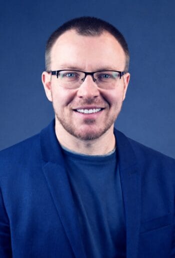 Dmitriy Fot, ein Vertreter von Ginmon, präsentiert sich in einem formellen Outfit vor einem einfarbigen Hintergrund. Die Herausforderungen der ZfA-Anbindung und die Integration von Sidecar-Lösungen stehen im Fokus der Diskussion über Altersvorsorgeprodukte bis zur Deadline 2027.