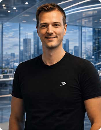 Ralf Heim, apoera.ventures, Sprecher auf der KI Exchange, präsentiert sich in einem modernen Büro mit Glaswänden und urbanem Hintergrund. Sein schwarzes T-Shirt und der freundliche Ausdruck vermitteln Professionalität und Zugänglichkeit in einem dynamischen Umfeld.