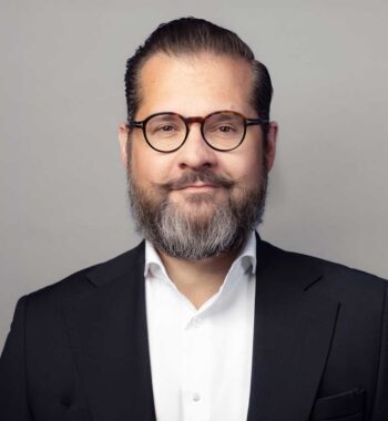 Eric A. Leuer, Manager bei Cofinpro, präsentiert sich in einem formellen Outfit. Sein Blick ist freundlich und selbstbewusst. Die Darstellung unterstreicht die Relevanz von Agentensystemen in der Automatisierung von Finanzinstituten und deren organisatorischen Herausforderungen.