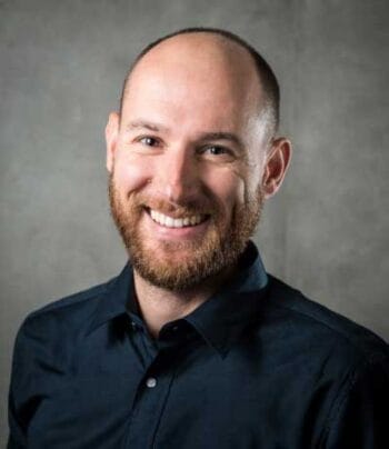 Antoine Coetsier, COO von Exoscale, wird in einem professionellen Porträt abgebildet. Er trägt ein dunkles Hemd und hat einen gepflegten Bart. Der Hintergrund ist neutral und hebt die Person hervor, die freundlich lächelt.