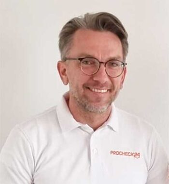 Daniel Hering, Geschäftsführer Vertrieb & Marketing bei Procheck24, präsentiert sich in einem weißen Poloshirt mit dem Logo von Procheck24. Der Hintergrund ist neutral, was den Fokus auf die Person lenkt.