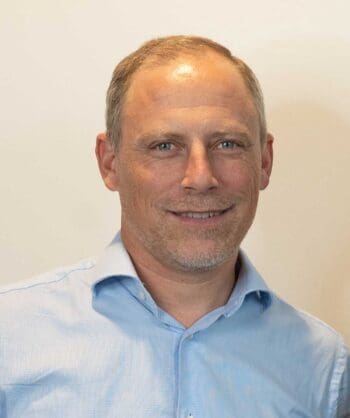 Ein Mann mit kurzen, grauen Haaren und einem leichten Bart lächelt in die Kamera. Er trägt ein hellblaues Hemd. Die AMLA wird in der Lage sein, Lücken im Audit-Log zu identifizieren und zu analysieren.
