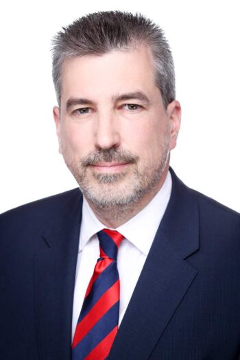 Elmar Kühn, Uniti-Hauptgeschäftsführer, präsentiert sich in einem formellen Anzug mit gestreifter Krawatte. Der Hintergrund ist neutral gehalten, was den Fokus auf seine Person lenkt. Sein Gesichtsausdruck vermittelt Professionalität und Entschlossenheit.