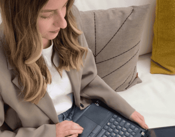 Eine Person arbeitet an einem Laptop, während sie auf einem Sofa sitzt. Im Hintergrund sind zwei Kissen sichtbar. Die HUK-Coburg bietet nun digitale Rechtsschutz-Schadenmeldungen an, um Kunden in emotional belastenden Situationen schneller zu unterstützen.
