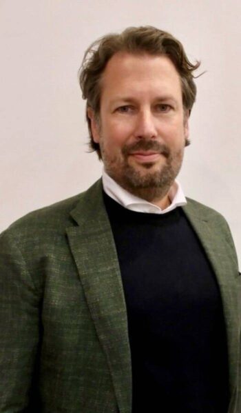 Manuel Sandhofer, General Manager - EMEA, Wise Platform, präsentiert sich in einem professionellen Umfeld. Sein Outfit besteht aus einem dunklen Pullover und einem grünen Blazer, was auf eine formelle, aber moderne Erscheinung hinweist.