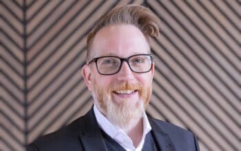 Henning Dittmer, RVP DACH von Ping Identity, präsentiert sich in einem professionellen Umfeld. Sein Auftreten spiegelt seine mehr als 20-jährige Erfahrung im Bereich Enterprise Sales und SaaS-Lösungen wider. Der Hintergrund ist modern und strukturiert.