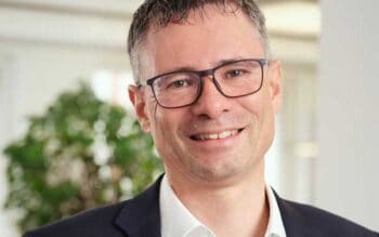 Stephan Schweizer, Executive Master in Information Technology, präsentiert sich in einem professionellen Umfeld. Seine Expertise im Bereich Sicherheitslösungen ist relevant für die Entwicklung offener Banking-Ökosysteme. Der Hintergrund zeigt eine grüne Pflanze, die eine angenehme Atmosphäre schafft.