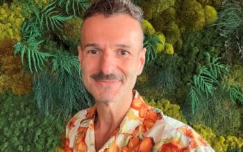 Thorsten Bambey, Head of AI Applications bei der Finanz Informatik, präsentiert sich vor einer grünen, pflanzenartigen Wandgestaltung. Der Hintergrund hebt die Verbindung zur Natur hervor, während sein farbenfrohes Hemd einen kreativen Akzent setzt. S-KIPilot wird im Kontext seiner
