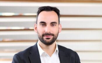 Alejandro Leal, Lead Analyst bei KuppingerCole, wird in einem professionellen Umfeld abgebildet. Er trägt einen schwarzen Anzug und hat einen neutralen Gesichtsausdruck. Der Hintergrund besteht aus horizontalen, hellen Streifen.