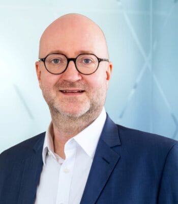 Michael Rodenberg, neuer Managing Director von Verisk Claims Solutions Germany, präsentiert sich in einem professionellen Umfeld. Er trägt einen dunklen Anzug und eine helle Hemd. Der Hintergrund ist hell und modern gestaltet.