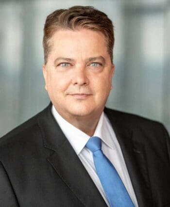 Christian Rhino, CIO der Privatkundenbank der Deutschen Bank, wird in einem professionellen Porträt abgebildet. Er trägt einen Anzug mit Krawatte und blickt direkt in die Kamera, was seine Rolle in der technologischen Transformation der Bank unterstreicht.