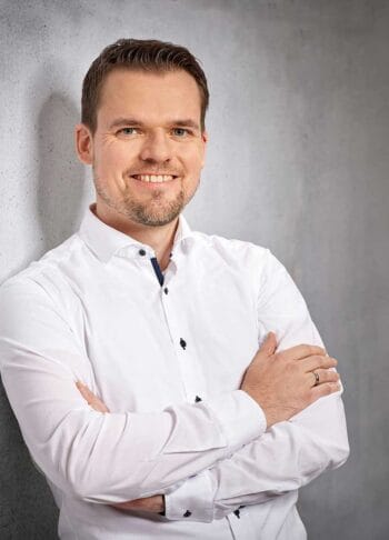 Dr. Markus von Detten, Senior Consultant PKI bei Achelos, präsentiert sich mit verschränkten Armen und einem Lächeln. Sein professionelles Auftreten unterstreicht die Bedeutung von Anforderungen in der Sicherheitsarchitektur, insbesondere im Kontext der DORA-Regulierung.