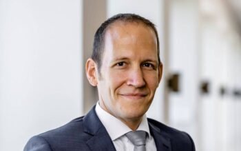Autor Jörg Botsch, PwC Deutschland, wird in einem professionellen Umfeld abgebildet. Er trägt einen Anzug und hat einen neutralen Gesichtsausdruck. Der Hintergrund ist hell und unscharf, was den Fokus auf seine Person lenkt.