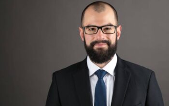 Robert Eberhard, Senior Manager bei PwC Deutschland, präsentiert sich in einem formellen Anzug mit Krawatte. Sein gepflegtes Erscheinungsbild und die Brille unterstreichen seine Professionalität im Bereich Cyber Security. Autor Robert Eberhard, PwC Deutschland.