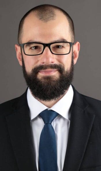 Robert Eberhard, Senior Manager bei PwC Deutschland im Bereich Cyber Security, präsentiert sich in formeller Kleidung. Die Darstellung unterstreicht die Bedeutung von Threat Modeling im Kontext der DORA-Verordnung zur Verbesserung der Sicherheitsstandards.