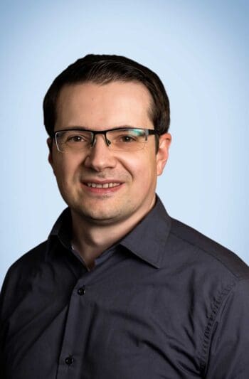 Sergius Mohr, Leiter der Produktentwicklung bei Fincon Reply, präsentiert sich in einem professionellen Umfeld. Seine Funktion unterstreicht die Relevanz der Diskussion über die Notwendigkeit strukturierter Schnittstellen im Kontext der KI-Entwicklung.