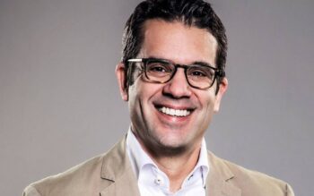 Peter Frey, Gründungspartner von Annerton, wird in einem professionellen Umfeld abgebildet. Er trägt einen hellen Blazer und ein weißes Hemd. Sein Lächeln und die Brille unterstreichen seine freundliche Ausstrahlung.