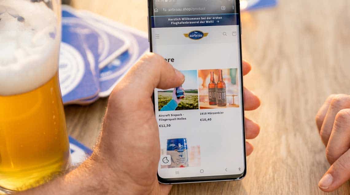 Ein Mobilgerät zeigt eine Online-Shop-Oberfläche mit verschiedenen Produkten, darunter Bier und Snacks. Im Kontext der Zahlungsinfrastruktur am Flughafen München wird Epay als zentraler Payment-Partner hervorgehoben, um die Effizienz zu steigern.