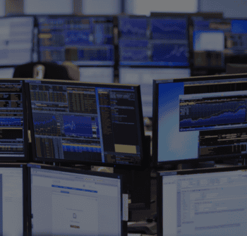 Mehrere Computerbildschirme in einem Handelsraum zeigen Finanzdaten und Marktanalysen. Die Baader Bank fungiert als depotführende Bank und Infrastrukturpartner der digitalen Vermögensverwaltung von DJE.