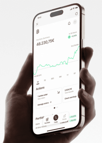 Ein Smartphone wird gehalten, auf dessen Bildschirm eine Portfolioübersicht von Bitpanda angezeigt wird. Der aktuelle Wert beträgt 48.230,75 €, mit einem Anstieg von 2,14 % in den letzten 24 Stunden. Grafische Darstellungen verdeutlichen die Entwicklung des Portfolios.