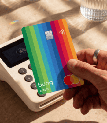 Hand mit Ring hält bunte bunq Kreditkarte an ein mobiles Kartenlesegerät.