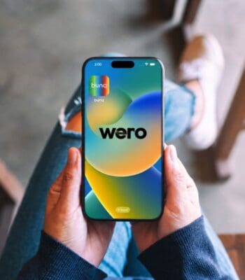 Ein Smartphone wird gehalten, auf dessen Bildschirm die bunq-App mit dem Logo „wero“ angezeigt wird. Die Benutzeroberfläche zeigt ein modernes, farbenfrohes Design. Der Hintergrund ist unscharf und vermittelt eine entspannte Atmosphäre.