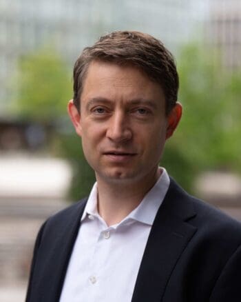 Steven Jacob, Partner bei Arkwright, steht im dunklen Sakko und weißen Hemd vor unscharfem Grün. Er spricht über den digitalen Euro und Wero.
