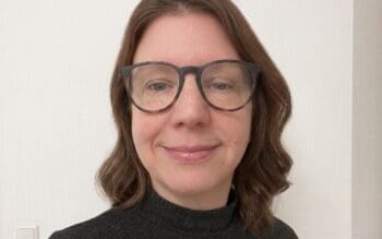 Erena Langley, Director of Regulatory Solutions bei Navex, mit dunkler Brille und schwarzem Rollkragen vor heller Wand; sie berät zu KI-Compliance in komplexen IT-Landschaften.