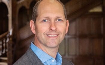 Greg Holmes, Field CTO EMEA bei Apptio, lächelt in Sakko und hellblauem Hemd vor einer hölzernen Innenraumkulisse. Seine Beratung verbindet Mainframe-Erfahrung mit schrittweiser Modernisierung.