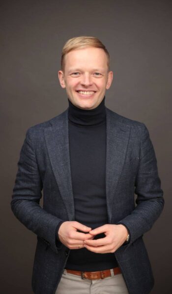 Jan Wichmann, Gründer von JWR Advisory, steht lächelnd mit ineinandergelegten Händen vor grauem Hintergrund; der Beitrag ordnet die Solaris-Strafe in die BaaS-Konsolidierung ein.