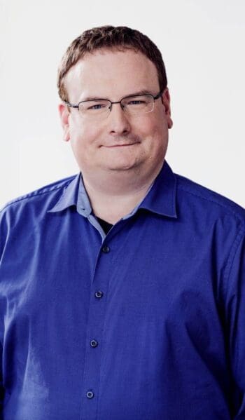 Matthias Thiele, Bereichsleiter Digital Products & Technology bei der DKB, präsentiert sich in einem blauen Hemd. Der Hintergrund ist neutral und hell, was die Professionalität und den Fokus auf seine Rolle im Unternehmen unterstreicht.